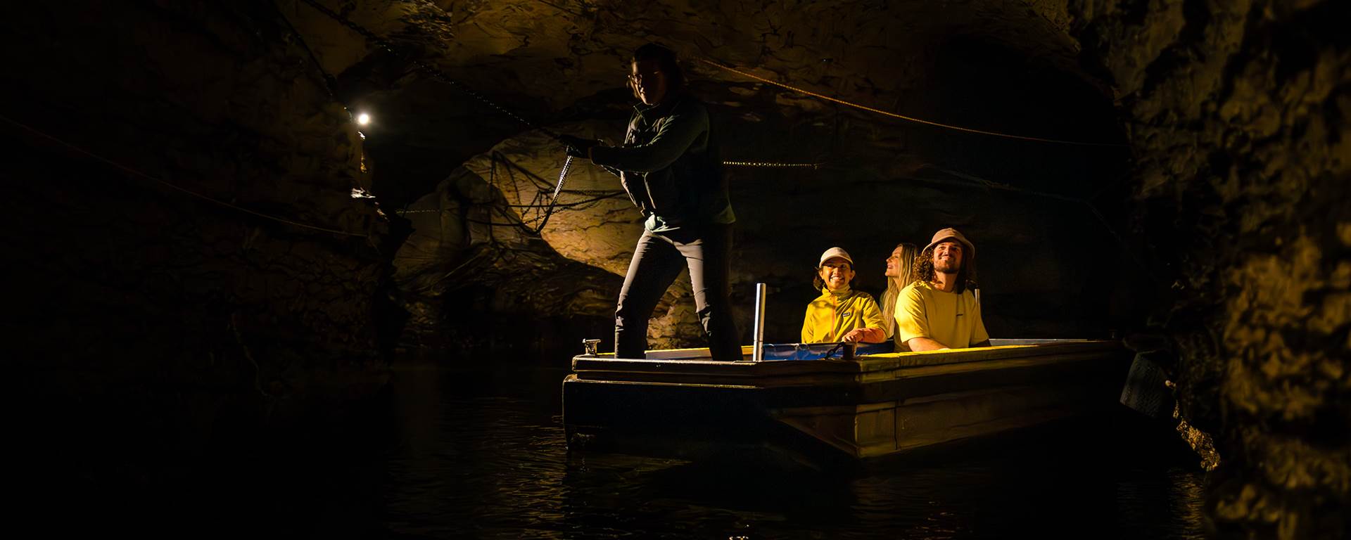 A group of three are guided through an underground cave on a small boat 