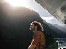 A man stands in the sunlight on the deck of a vessel cruising through Doubtful Sound