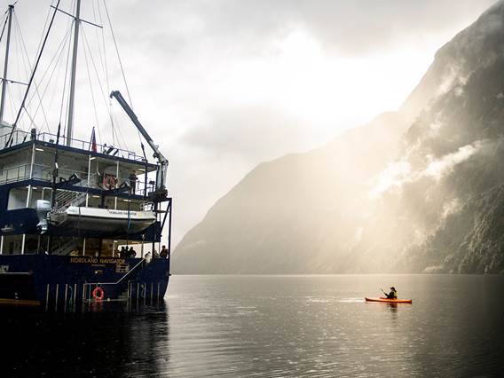 A kayaker floats near the Fiordland Navigator vessel on the water at Doubtful Sound