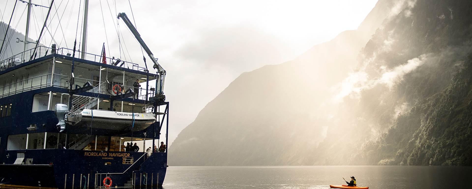 A kayaker floats near the Fiordland Navigator vessel on the water at Doubtful Sound