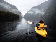 A bright yellow kayak floats along the water in gloomy Doubtful Sound 