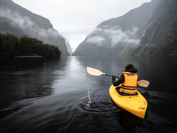 A bright yellow kayak floats along the water in gloomy Doubtful Sound 
