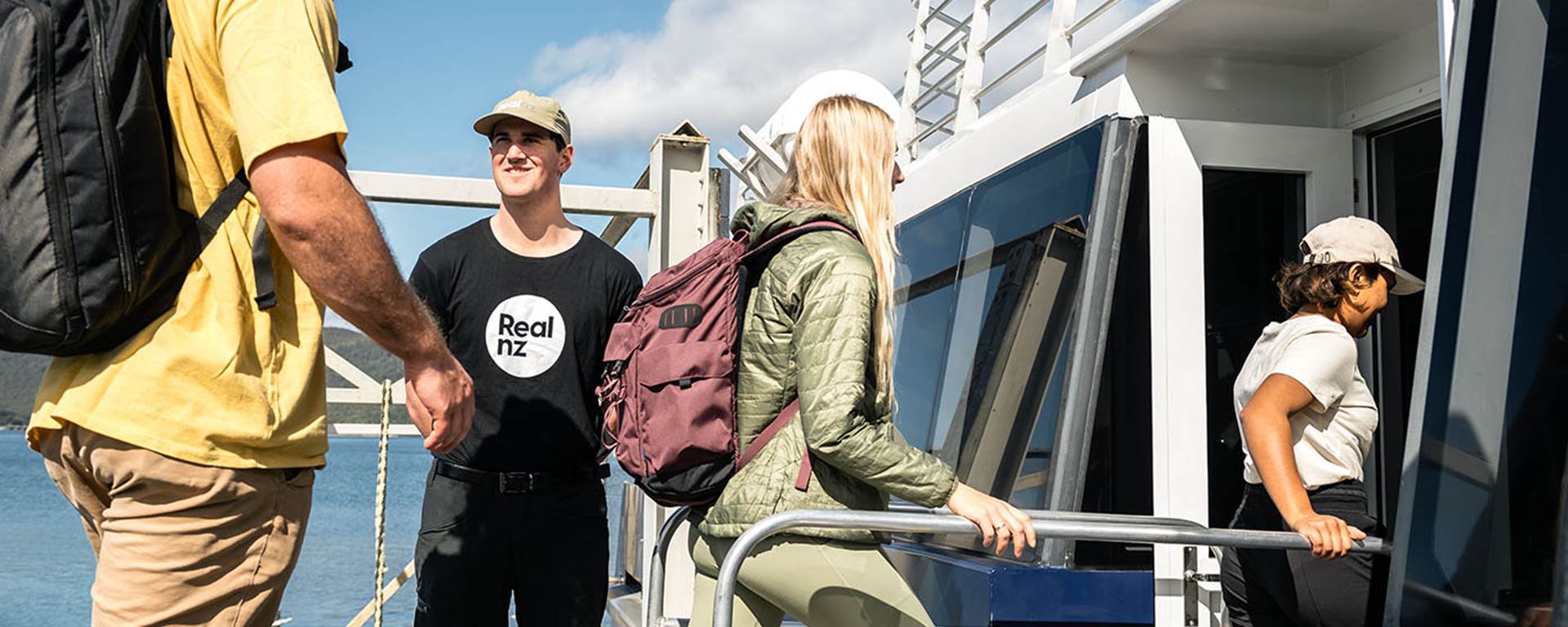 Three guests are welcomed on board a ferry by a friendly RealNZ employee